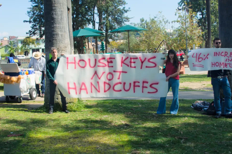 Two people holding sign that says "house keys not handcuffs" during an anti-homelessness event in Los Angeles, California